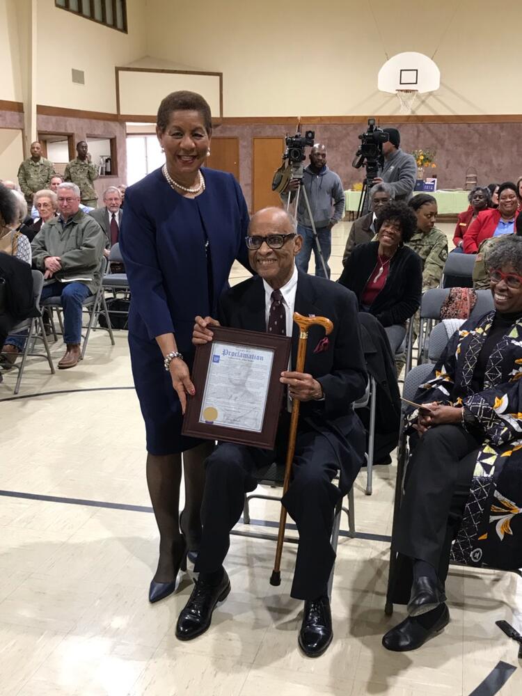 Mayor holding proclamation with seated man, Mr. Fulton Walker. 