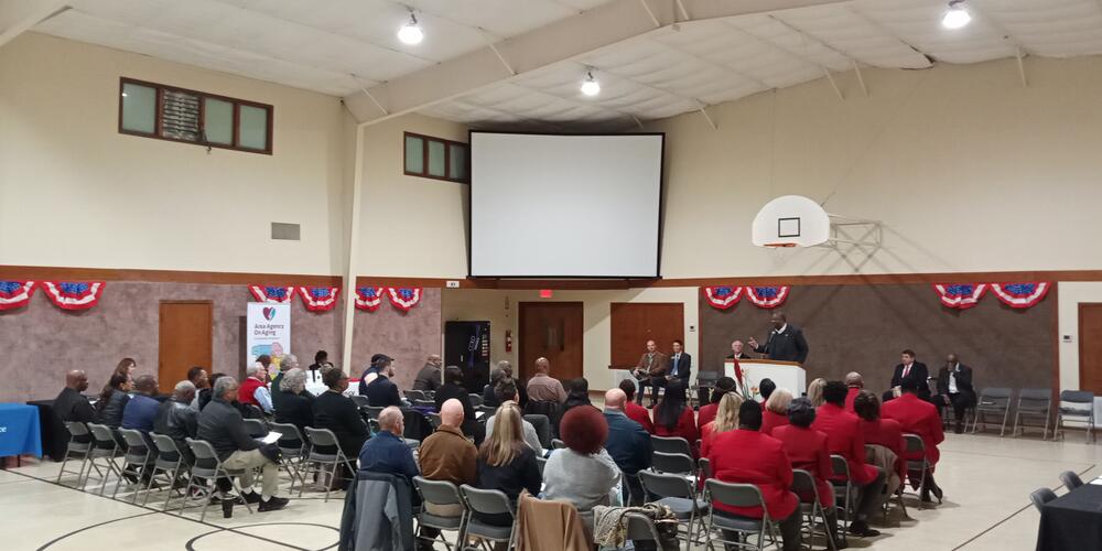 Crowd listening to speaker in  gym decorated with banners.